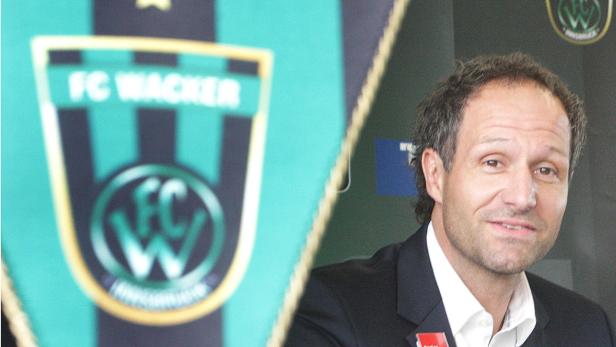 Ein Mann in einem Anzug steht neben einem Wimpel des FC Wacker Innsbruck.