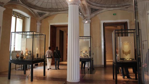 Ein Museumsraum mit antiken Artefakten in Vitrinen und Besuchern.