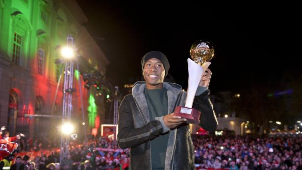 David Alaba hält eine Trophäe vor einer jubelnden Menschenmenge.