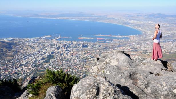 Eine Frau blickt von einem Felsen auf Kapstadt und die Küste.