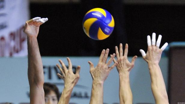 Mehrere Hände strecken sich nach einem gelb-blauen Volleyball.