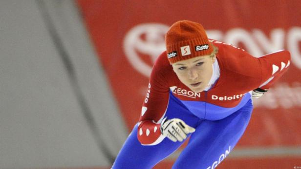 Eine Eisschnellläuferin in rot-blauer Wettkampfkleidung und Mütze auf dem Eis.