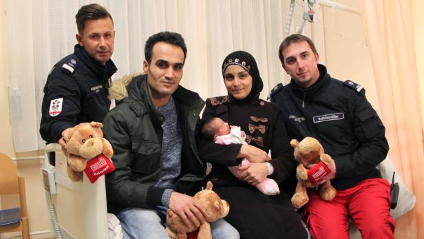 Eine Familie mit ihrem Neugeborenen, umgeben von zwei Notfallsanitätern mit Teddybären.