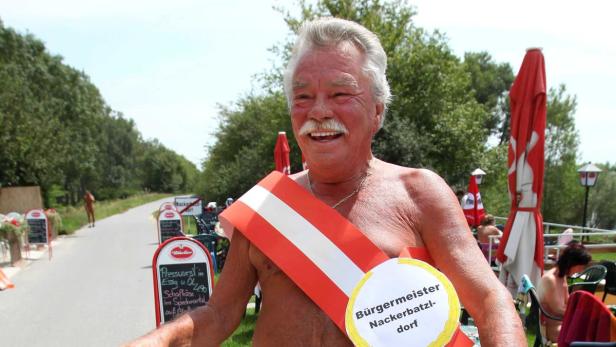 Ein Mann mit einer Schärpe mit der Aufschrift „Bürgermeister Nackerbatzldorf“ lächelt.