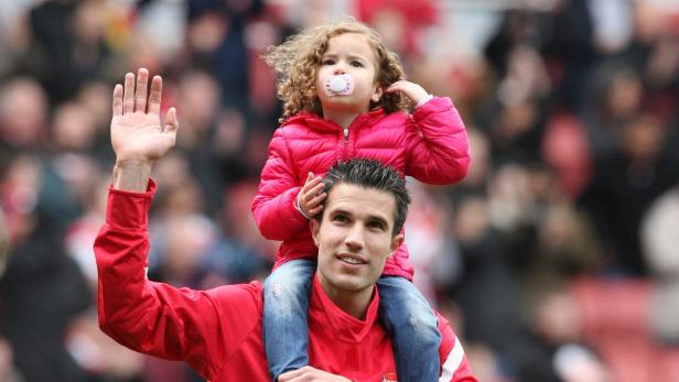 Ein Mann trägt ein kleines Mädchen mit Schnuller auf seinen Schultern und winkt.