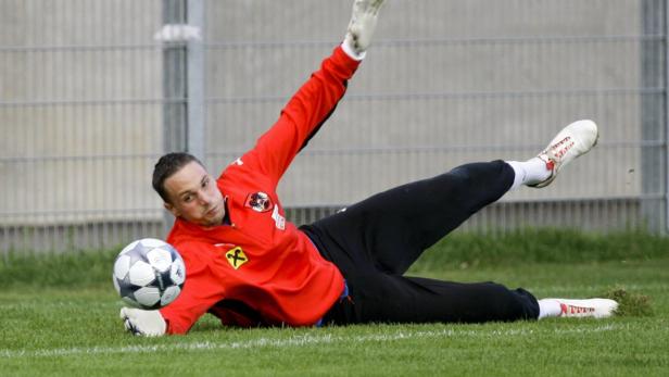 Ein Torwart in roter Sportkleidung hechtet nach einem Fußball.