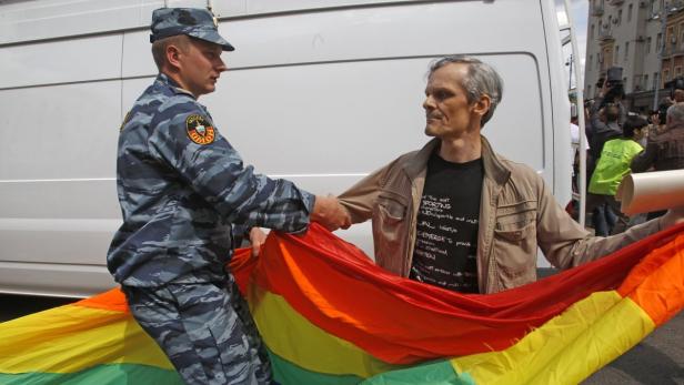 Ein Polizist hält eine Regenbogenflagge, die von einem Demonstranten gehalten wird.