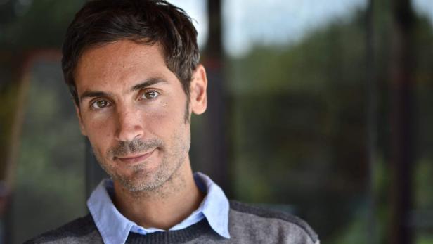 Ein Mann mit braunen Haaren und einem grauen Pullover blickt in die Kamera.