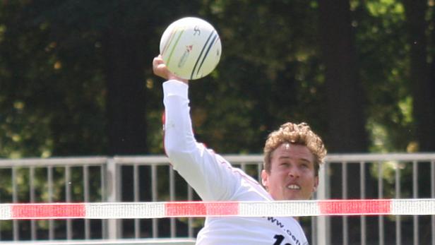 Ein Mann schlägt einen Ball beim Faustball über das Netz.
