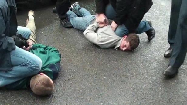 Zwei Männer werden von Polizisten auf dem Boden fixiert und gefesselt.