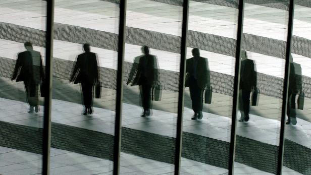 Mehrere verschwommene Spiegelbilder von Geschäftsleuten mit Aktentaschen, die über einen Zebrastreifen gehen.