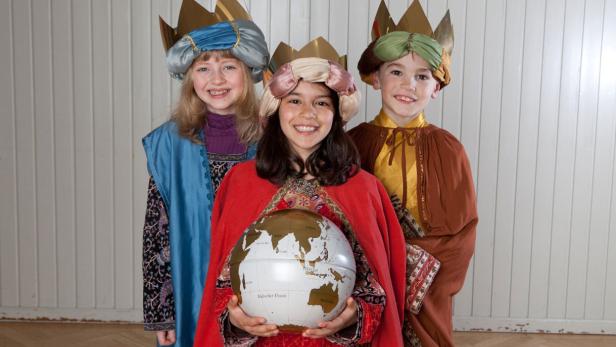 Drei Kinder, als die Heiligen Drei Könige verkleidet, halten einen Globus.