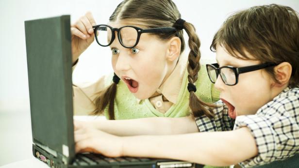 Zwei Kinder mit Brillen schauen überrascht auf einen Laptop.