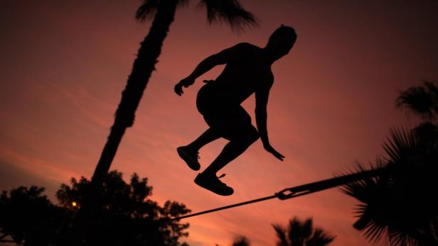 Die Silhouette eines Mannes, der bei Sonnenuntergang auf einer Slackline balanciert.