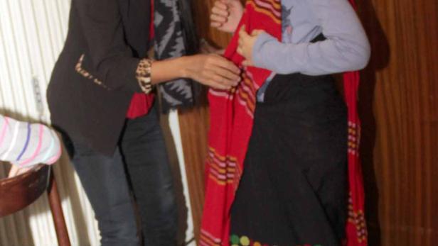 Eine Frau hilft einem Mädchen, ein traditionelles Kleid anzuziehen.