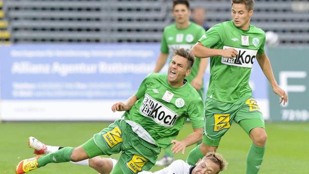 Ein Fußballspieler in Grün stürzt während eines Spiels zu Boden.