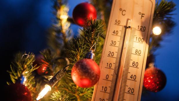 Ein Thermometer zeigt Temperaturen um den Gefrierpunkt an einem Weihnachtsbaum mit roten Kugeln.