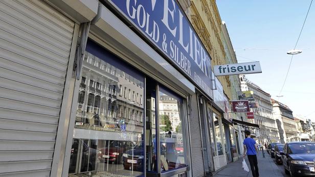 Ein Juweliergeschäft mit der Aufschrift „Gold & Silber“ und ein Friseursalon an einer Straße.