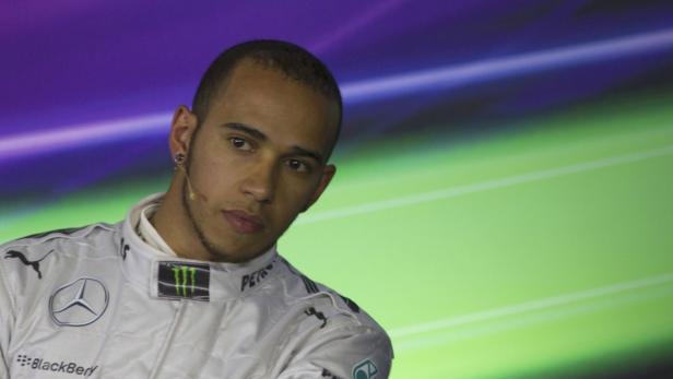 Lewis Hamilton in Rennfahrerkluft vor einem farbigen Hintergrund.
