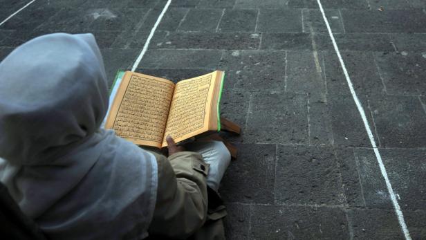 Eine Person liest den Koran auf einem gepflasterten Platz.
