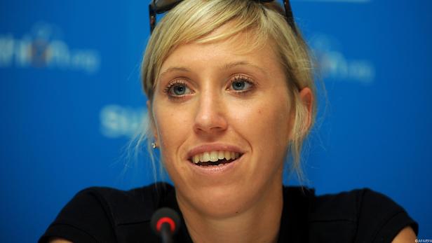 Eine blonde Frau mit blauen Augen spricht vor einem blauen Hintergrund.