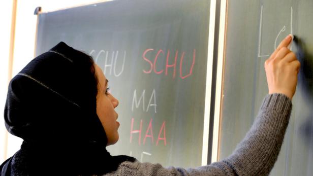 Eine Frau mit Kopftuch schreibt mit Kreide auf eine Tafel.