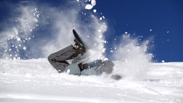 Ein Snowboardfahrer stürzt im Schnee, umgeben von Schneestaub.