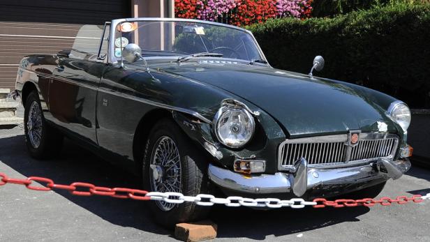 Ein beschädigter, dunkelgrüner MGB Roadster steht im Freien.