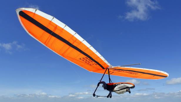 Ein orangefarbener Drachenflieger fliegt vor blauem Himmel.