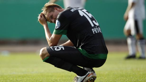 Ein enttäuschter Fußballspieler hockt auf dem Rasen und stützt seinen Kopf in den Händen.