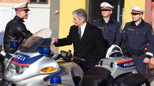 Ein Mann im Anzug schüttelt einem Polizisten die Hand, der auf einem Polizeimotorrad sitzt.