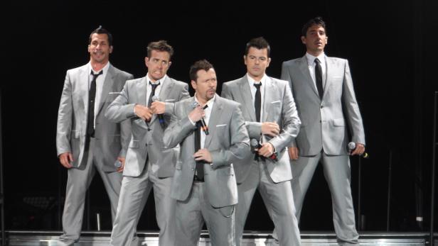 Die New Kids on the Block treten in grauen Anzügen auf einer Bühne auf.