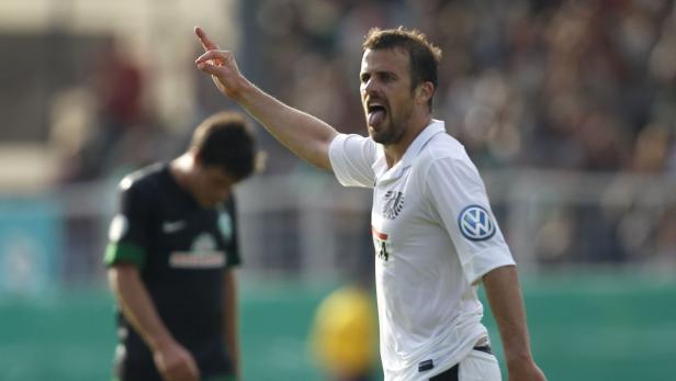 Ein Fußballspieler in weißem Trikot gestikuliert auf dem Spielfeld.