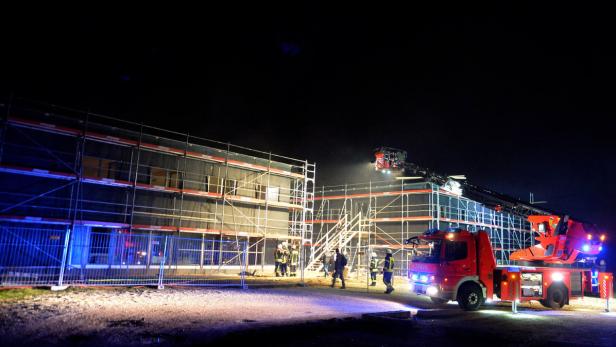 Ein rotes Feuerwehrfahrzeug steht vor einem Gebäude mit Baugerüst bei Nacht.