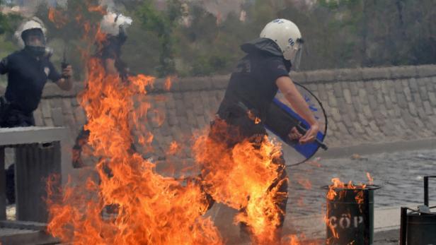 Polizisten stehen vor einem Feuer, einer hält einen Schild.