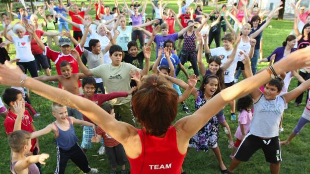 Eine Gruppe von Menschen, darunter viele Kinder, macht Gymnastik im Freien.