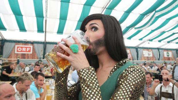 Conchita Wurst trinkt aus einem großen Bierkrug in einem Festzelt.