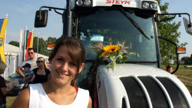 Eine junge Frau steht vor einem Steyr-Traktor mit Blumenschmuck.