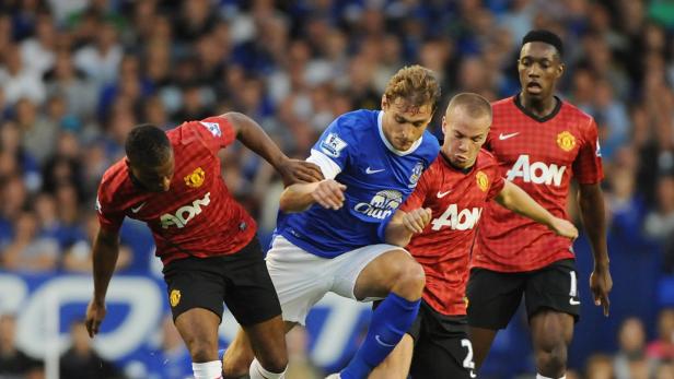 Ein Fußballspieler im blauen Trikot wird von drei Gegenspielern in roten Trikots bedrängt.