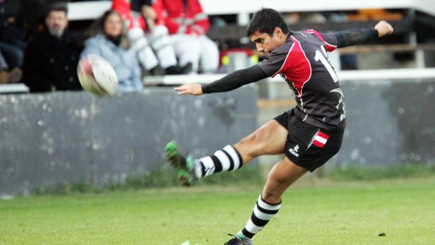 Ein Rugbyspieler tritt einen Rugbyball auf einem grünen Feld.