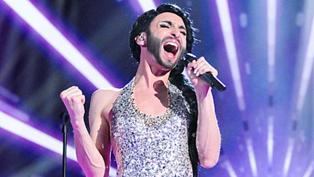 Conchita Wurst singt mit erhobener Faust auf einer Bühne.
