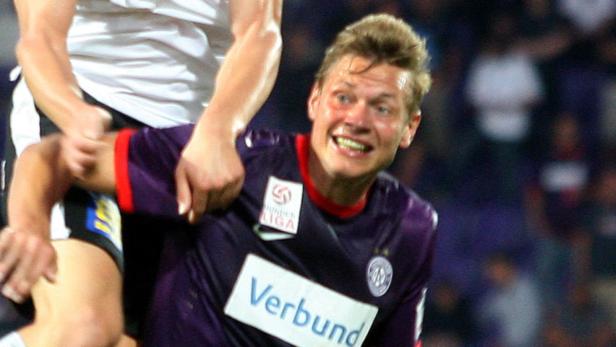 Ein Fußballspieler im lila Trikot wird von einem Gegenspieler festgehalten.