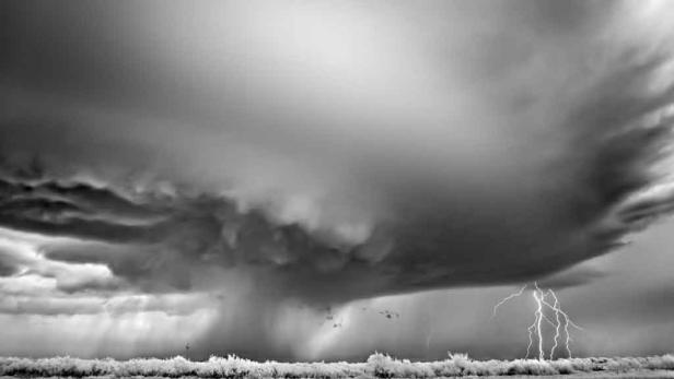 Ein Gewitter mit Blitzen zieht über eine Küstenlandschaft hinweg.