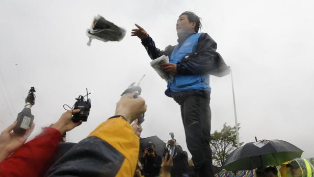 Ein Mann wirft Zeitungen in die Luft, während Reporter ihn fotografieren.