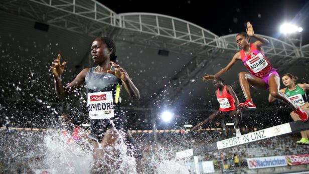 Mehrere Athletinnen springen während eines Hindernisrennens über einen Wassergraben.