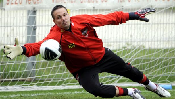 Ein Torwart in roter Jacke wehrt einen Fußball ab.