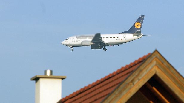 Ein Lufthansa-Flugzeug fliegt über ein Haus mit rotem Ziegeldach.