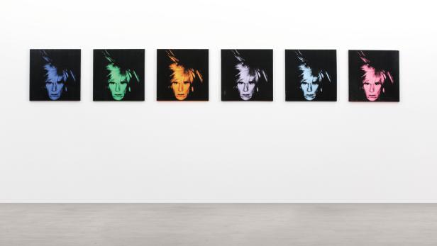 Sechs farbige Porträts von Andy Warhol hängen an einer weißen Wand.