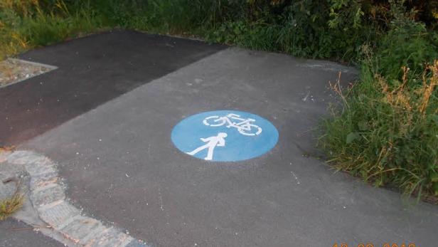 Ein blaues Schild auf einem Weg kennzeichnet einen kombinierten Fuß- und Radweg.