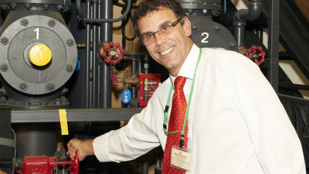 Ein Mann mit Brille und Krawatte bedient ein Ventil in einer Industrieanlage.